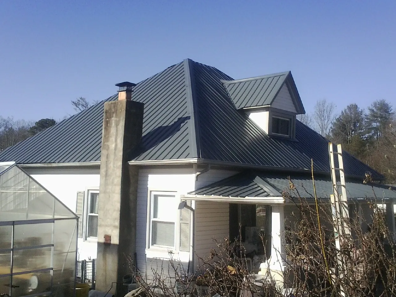 Dark blue standing seam metal roof on a white farmhouse with dormer — Slate & Tile Roof Repair by Roofing Brothers in Belton