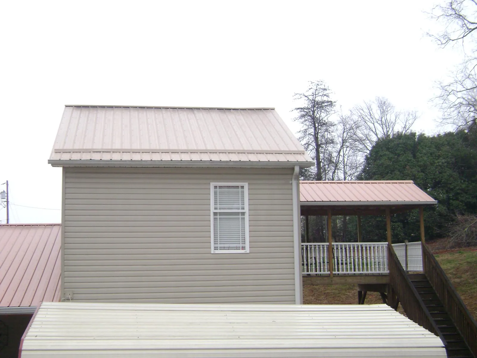 Tan metal roofs on a two story addition and attached porch, from a Roof Replacement job in Belton